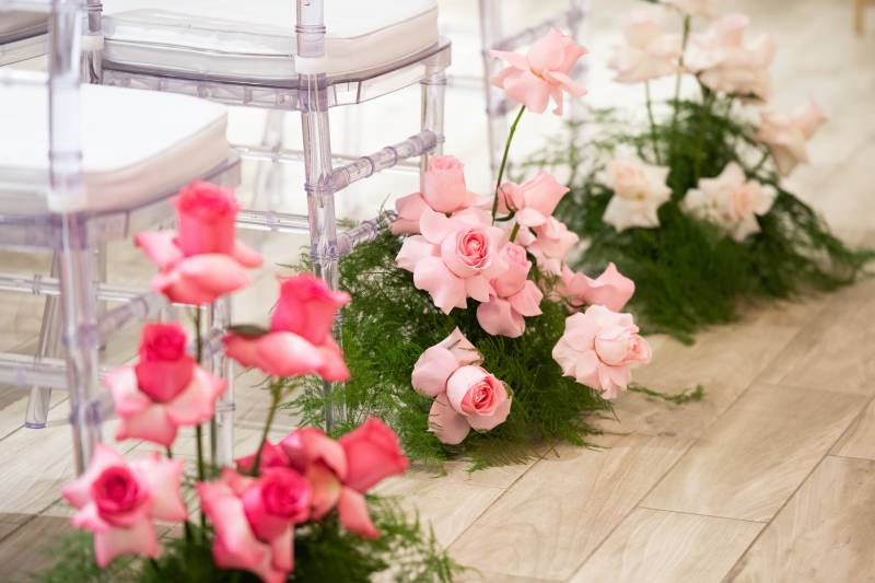 Pink and white flowers at edge of clear framed  seats with white cushions 