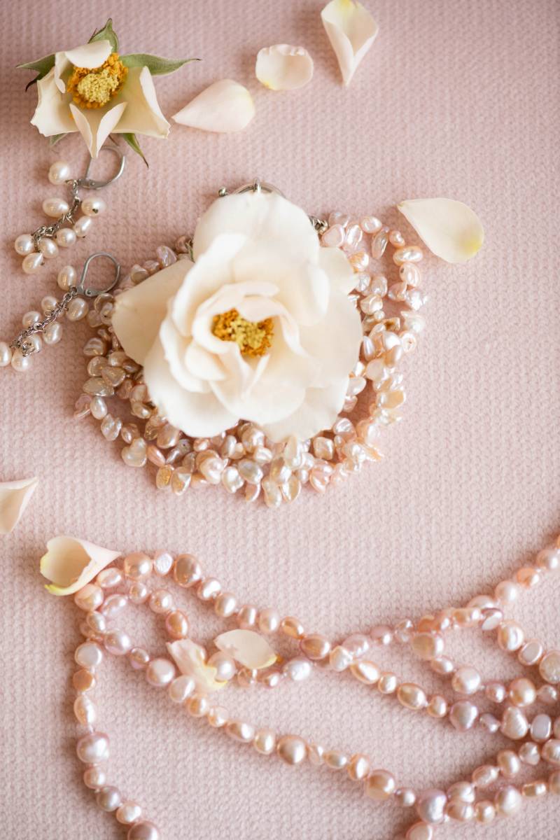 Blush pink necklaces surrounding white flower on pink surface