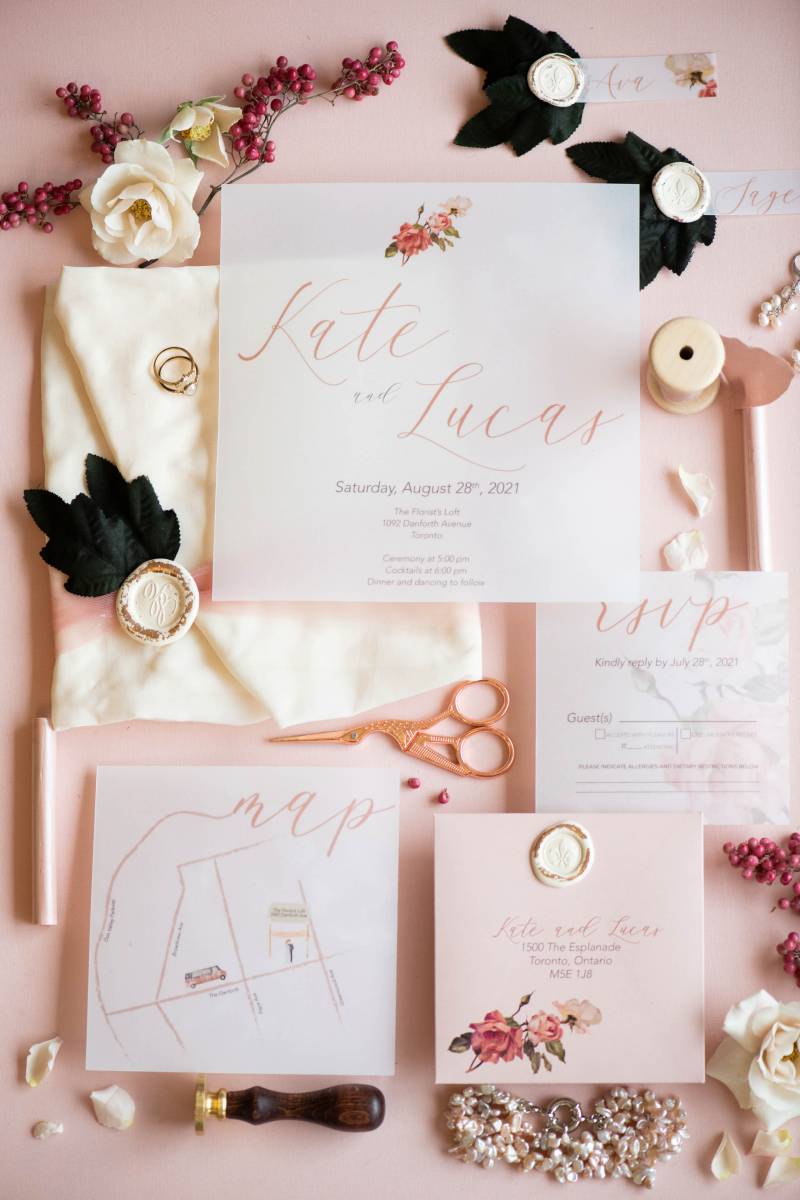 Wedding invitation flat lay on pink surface with red berries and black accents 