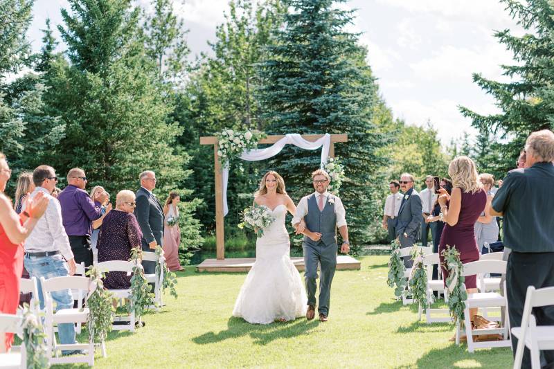 Bride and groom walking down aisle in arms while guests applaud 