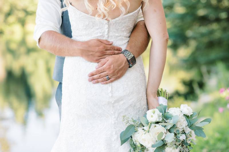 Groom embraces bride around her waist holding bouquet 