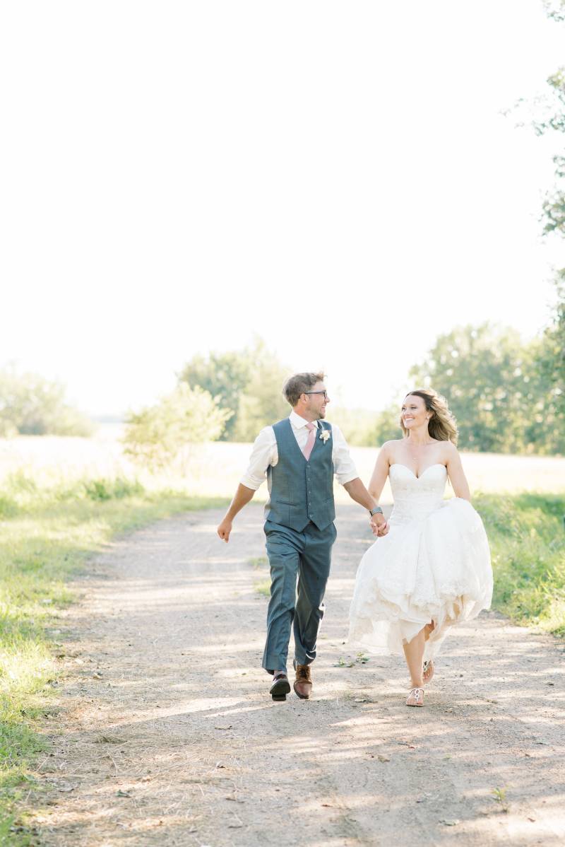 Bride and groom skip down gravel pathway holding hands 