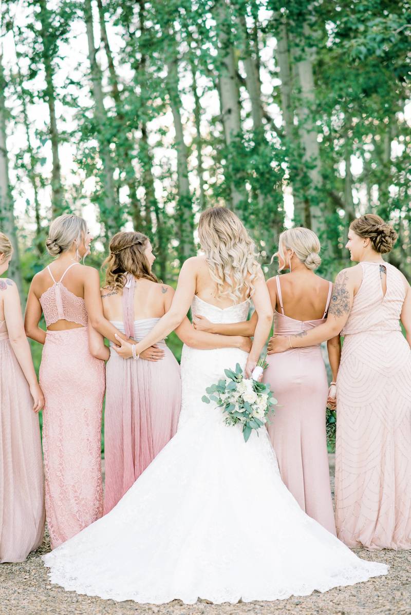 Bride and Bridesmaids stand facing away arms around backs 
