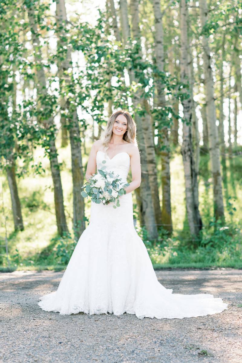 Bride in white dress smiling holding white bouquet on dirt path 